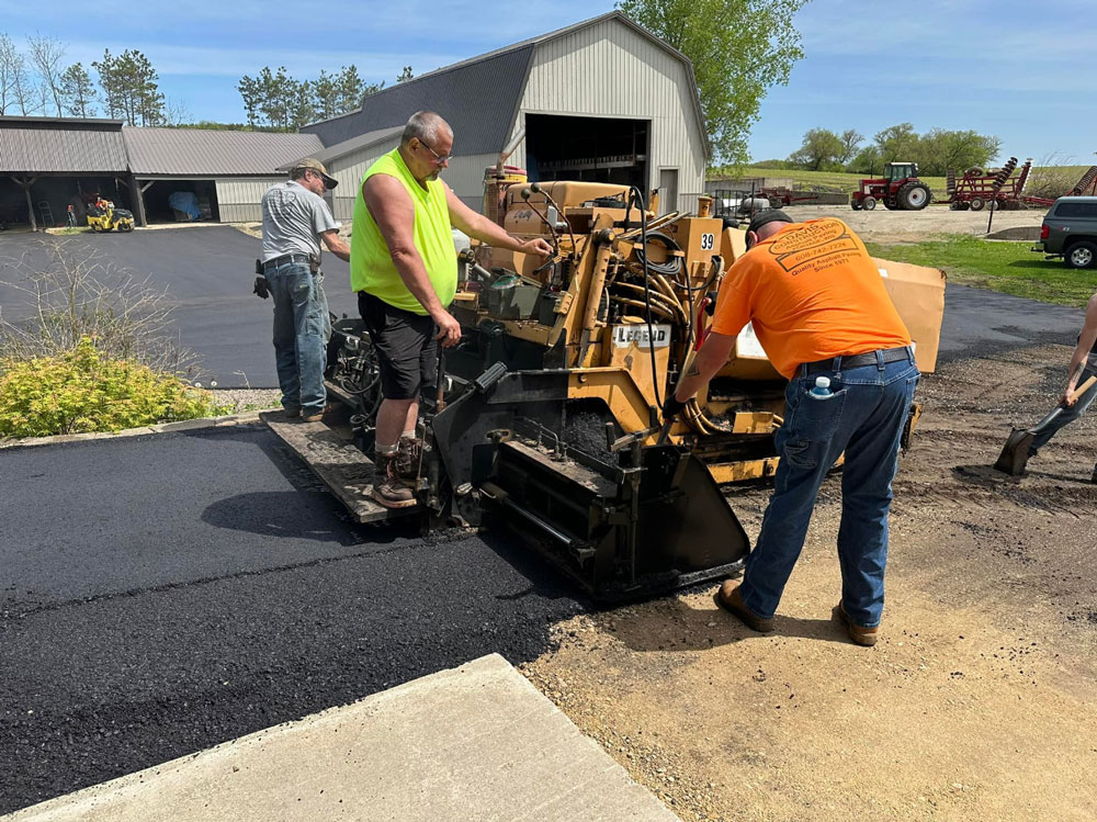 Davis-construction-workers-laying-asphalt Davis Construction workers lay asphalt with a paving machine in a rural setting.